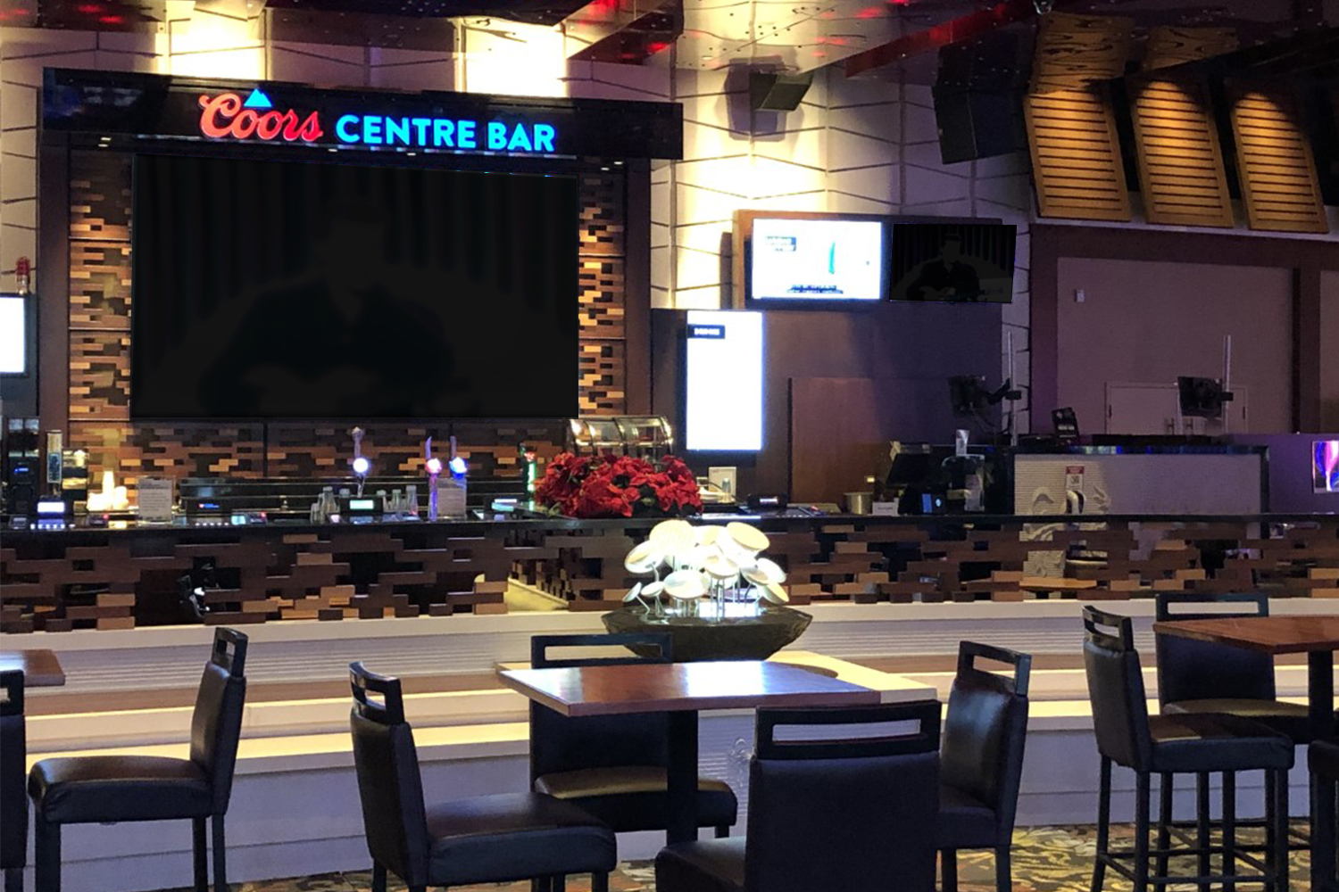 Tables and chairs and large TV screen and serving area in the background with Coors Centre Bar logos on top